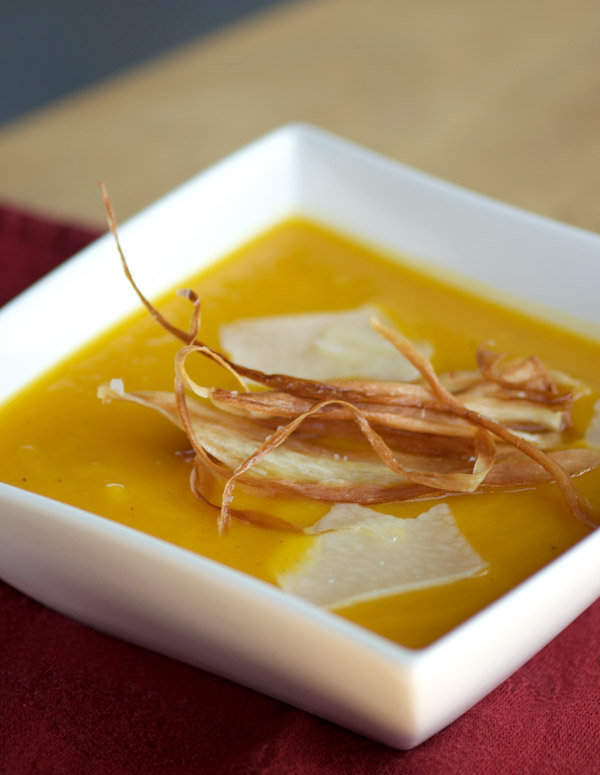 Bowl of glorious golden soup topped with Parmigiano Reggiano cheese and parsnip chips